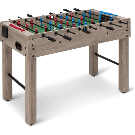 A wooden foosball table with a light gray-brown wood-grain finish, featuring a green playing field, red and blue player figures, black handles, and a white soccer ball on a clean white background.