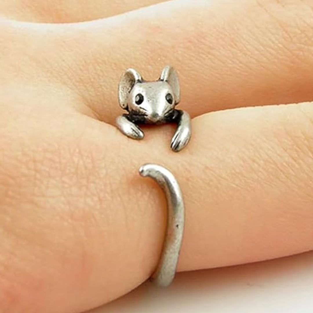 A silver-toned metal ring shaped like a small mouse or squirrel, worn on a person's finger. The ring has detailed features including ears, eyes, paws, and a curved tail, shown against the skin of the hand.