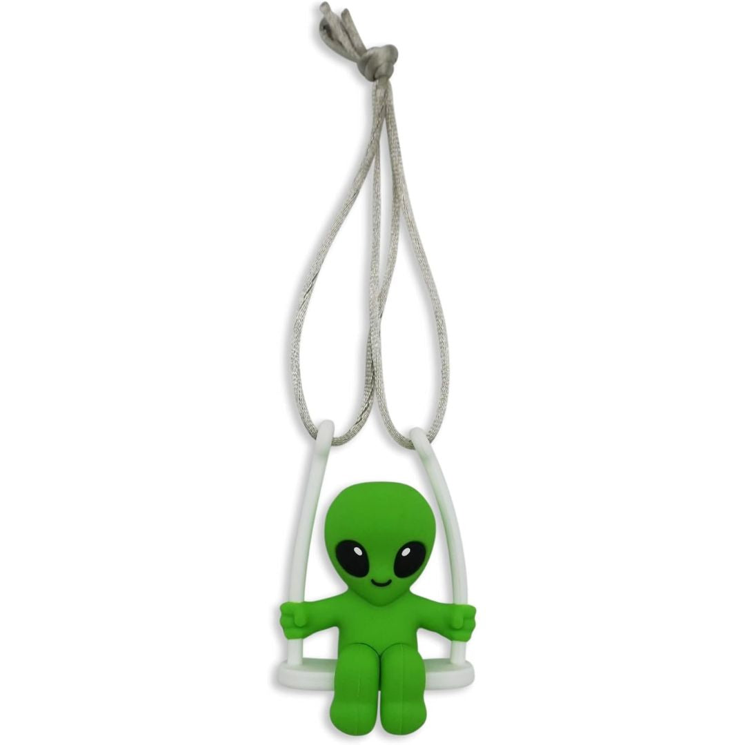 A green alien-shaped car charm with large black eyes sitting on a white swing, suspended by a white cord, shown against a plain white background.