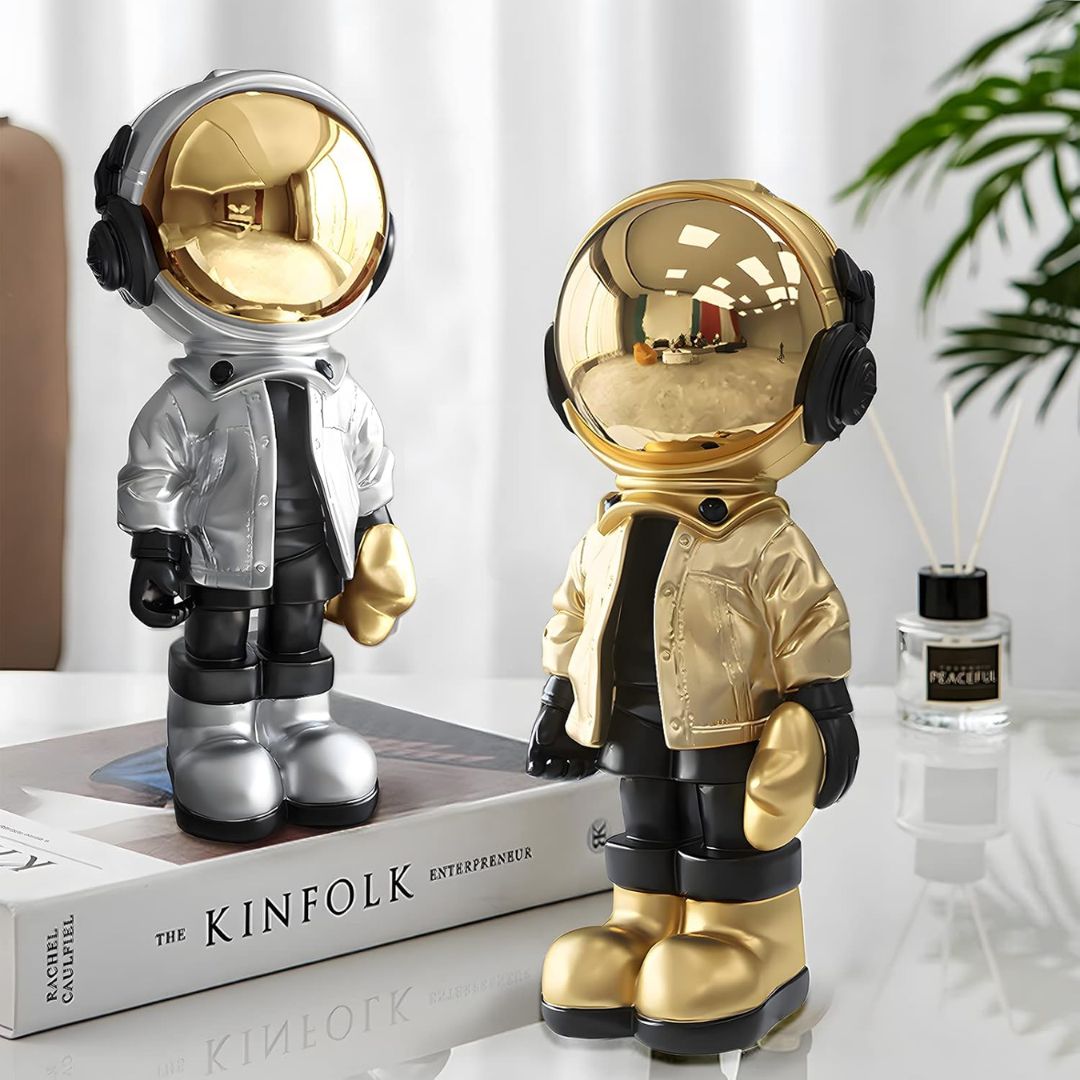 Silver and gold astronaut figurines on a table with curtains in the background.