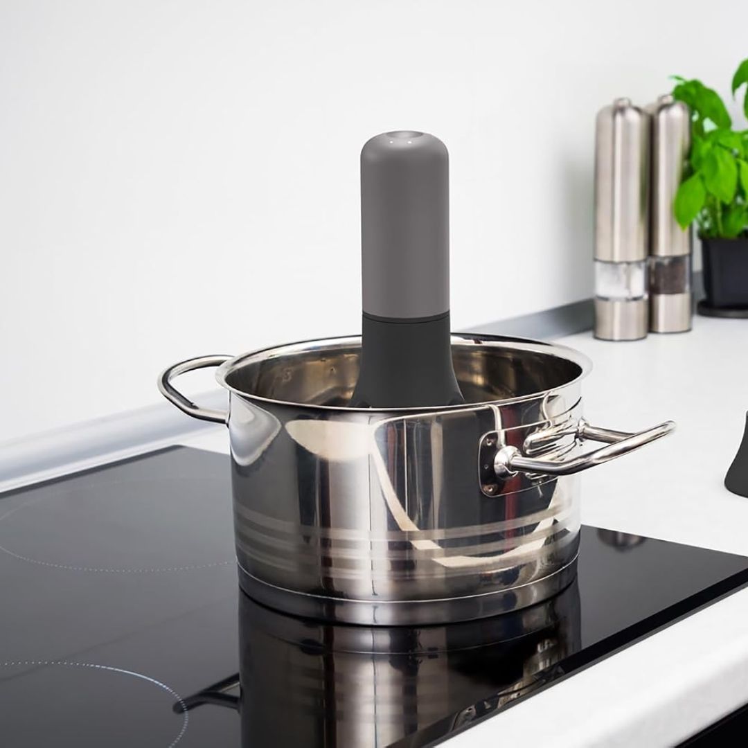 An automatic pan pot stirrer in a silver saucepan on a stove in a kitchen scenario
