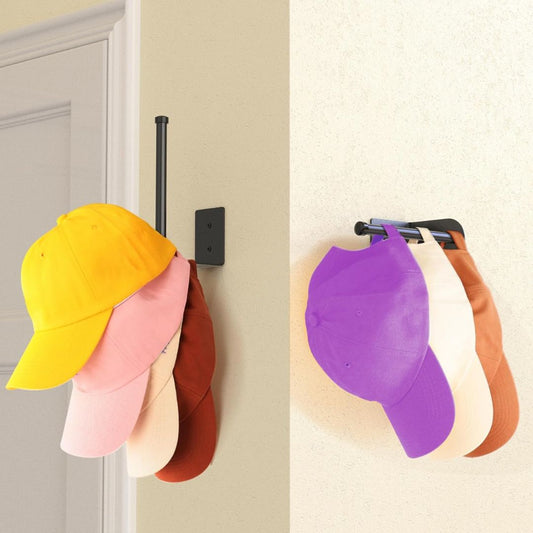 A black wall-mounted hat rack shown in two interior settings, holding a stack of baseball caps. The left rack is attached to a beige wall next to a white door and holds yellow, pink, cream, and brown caps.
