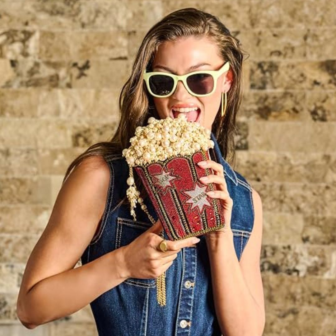 A woman holding a handbag made with pearls and red beadwork shaped like a bucket of popcorn.
