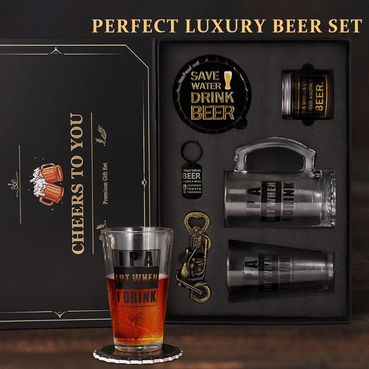 A premium beer-themed gift set displayed in an open black box, featuring engraved glassware, a small bottle, a keychain, and accessories. The set includes a clear handled beer mug, two clear tumblers with black lettering, a black bottle cap with gold text, and a small black bottle.