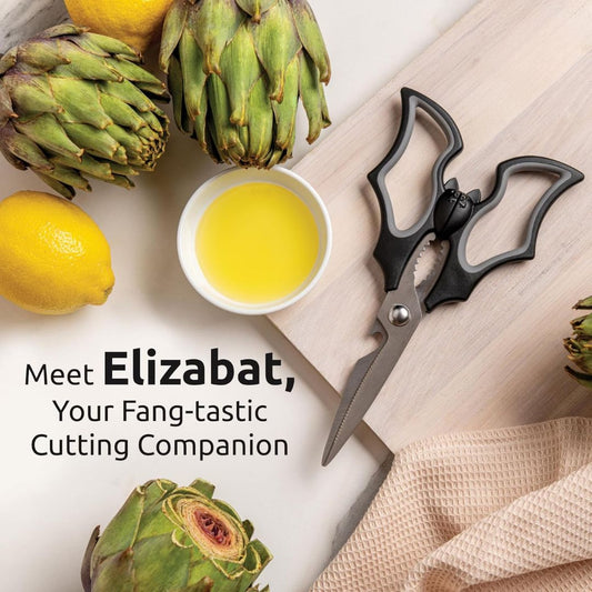 Bat shaped kitchen scissors with artichokes, lemons, and olive oil on a light background.