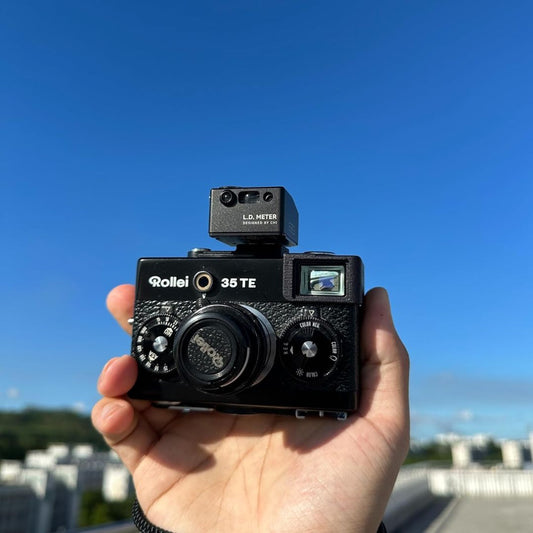 Black CHI L.D. Light Meter Pro mounted on a vintage Rollei film camera held outdoors against a blue sky