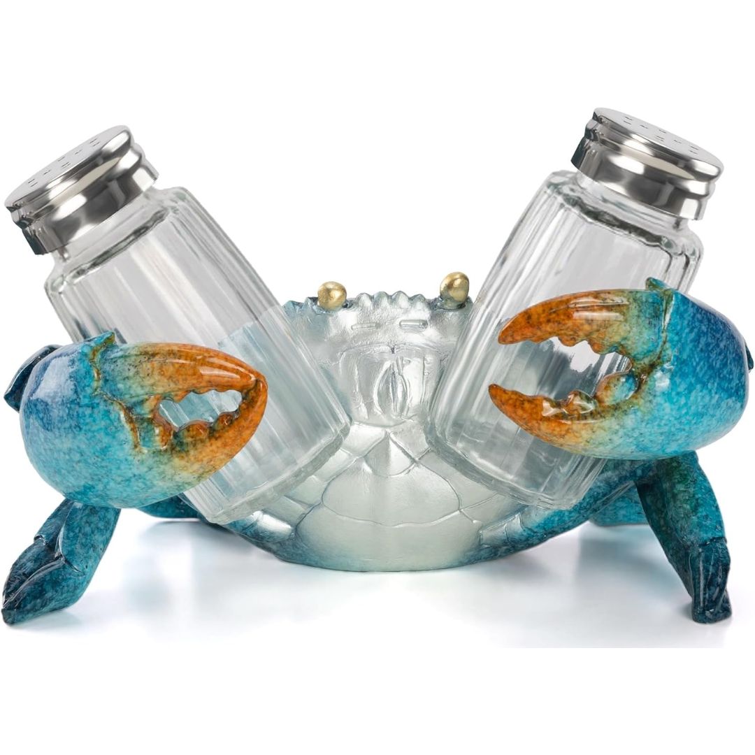 A decorative salt and pepper shaker set holder shaped like a crab, with two clear glass bottles and silver metal caps mounted on a blue crab body with orange claws, photographed on a white background.
