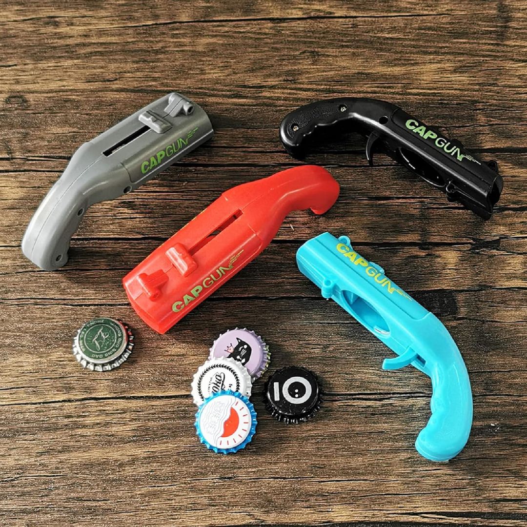 Four bottle cap launcher guns with bottle caps nearby on a wooden surface