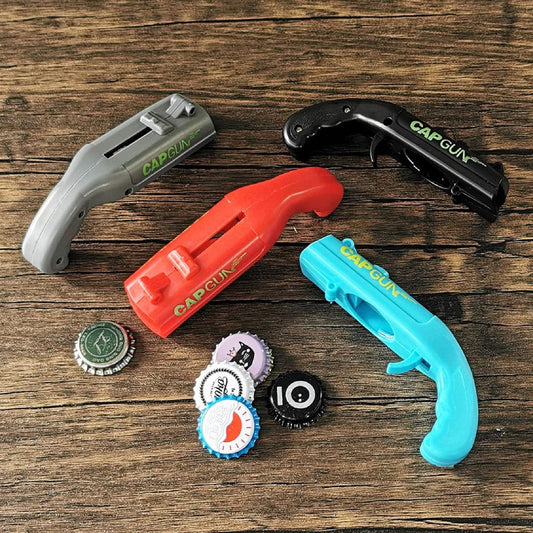 Four bottle cap launcher guns with bottle caps nearby on a wooden surface