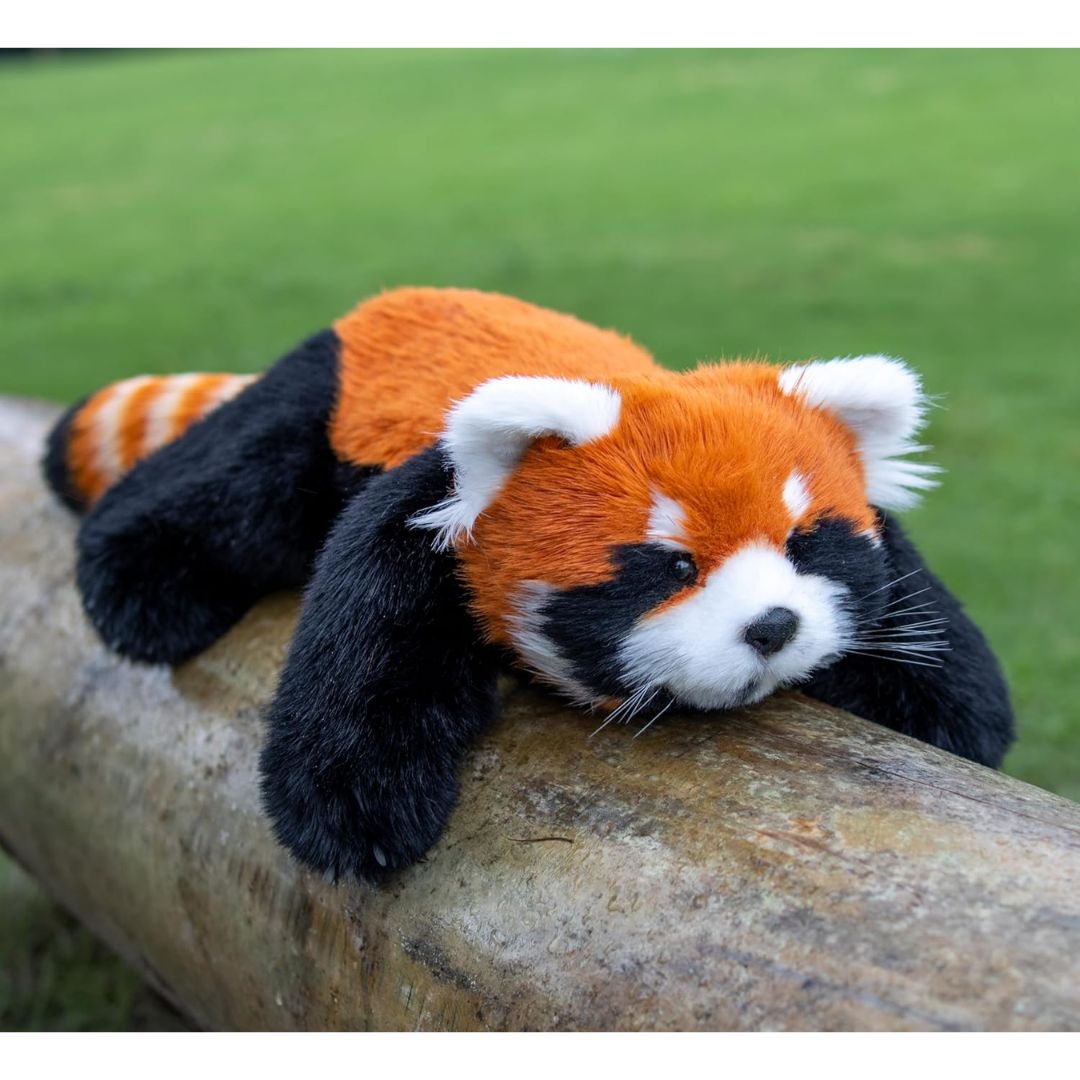 An interactive toy stuffed red panda on a wooden log with a grassy background.