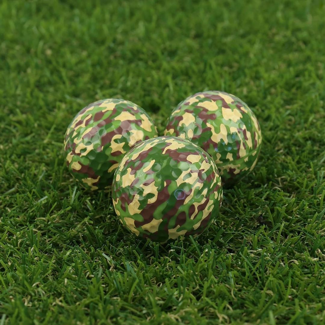 Three camouflage-patterned golf balls on a grassy surface