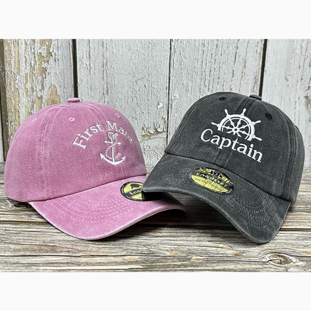 Pink and gray baseball caps with 'First Mate' and 'Captain' text on a wooden surface.