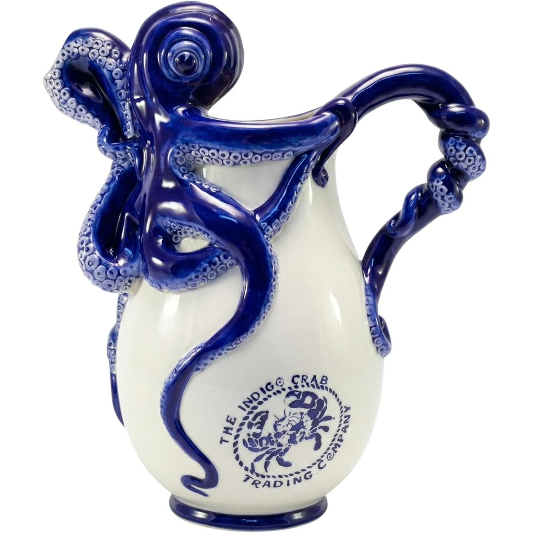 A ceramic pitcher shaped like an octopus wrapping around the vessel, with a glossy white body and deep cobalt blue octopus arms and printed branding. The front shows the text 'THE INDIC CRAB TRADING COMPANY' with a crab emblem.