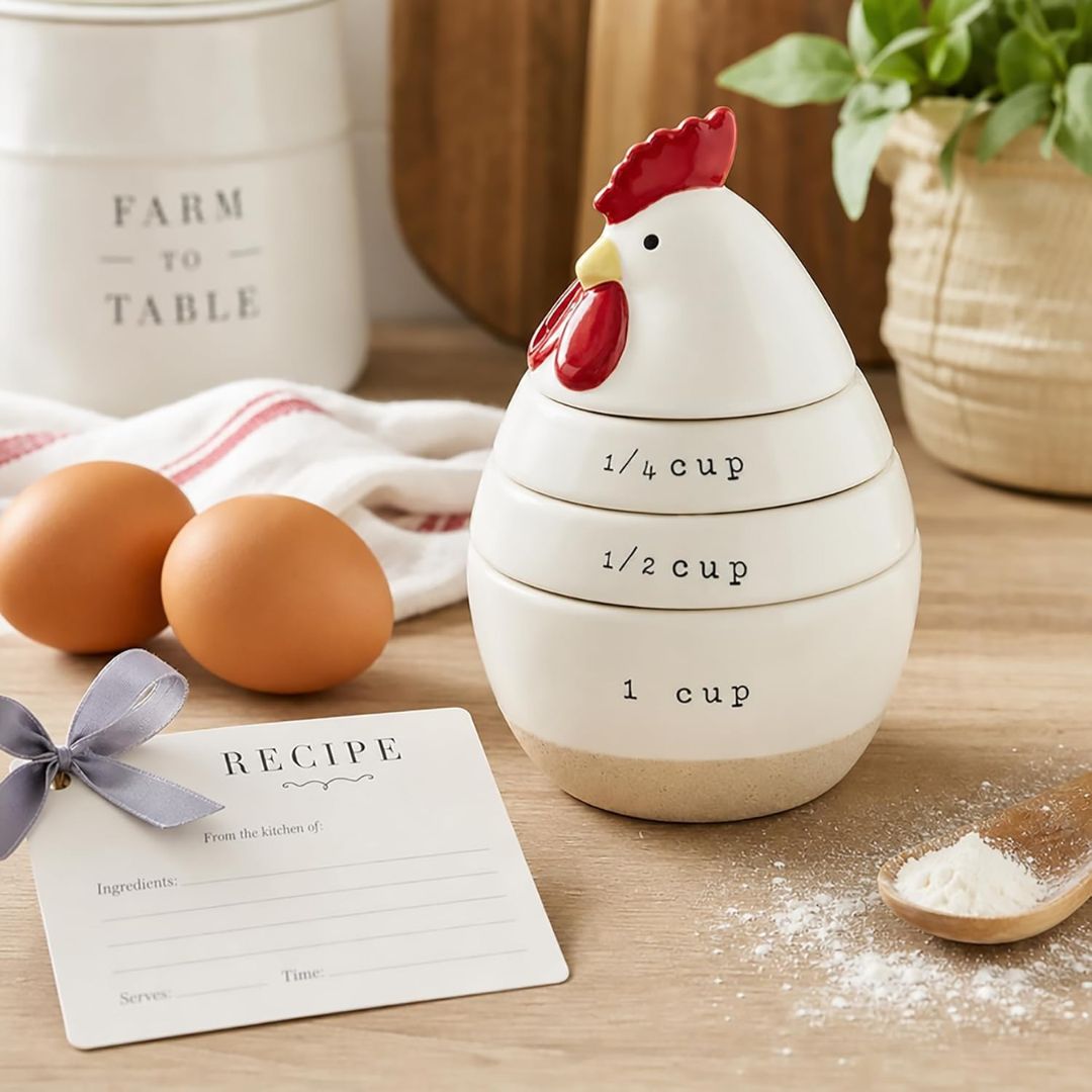 A ceramic egg-shaped measuring container set with stacked cups labeled 1/4 cup, 1/2 cup, and 1 cup, styled on a wooden table with eggs, a recipe card, and kitchen props.