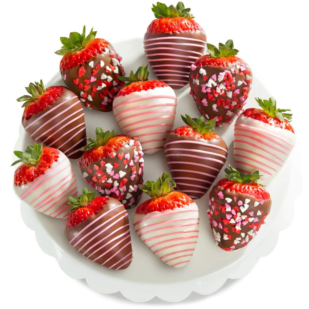 A group of chocolate-dipped strawberries arranged on a white scalloped plate against a clean white background. The strawberries are coated in dark and milk chocolate with some decorated in pink and white sprinkles.