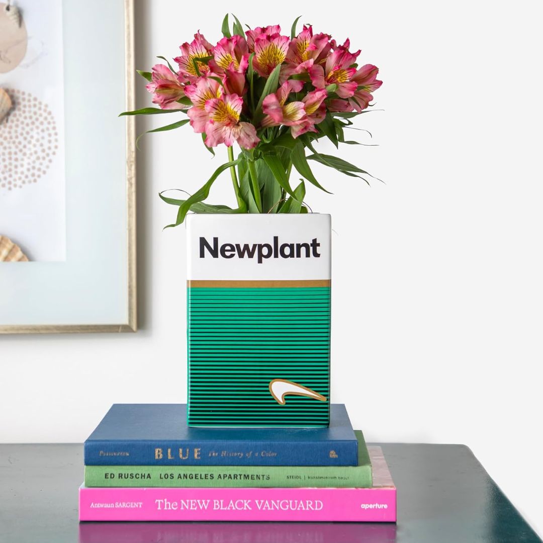 Retro cigarette pack-style ceramic vase filled with pink flowers and displayed on stacked books