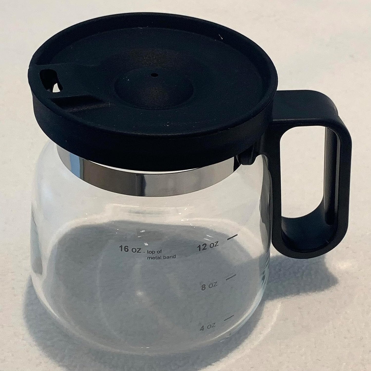 Clear glass coffee carafe which is a mug with black lid and handle on a light gray background