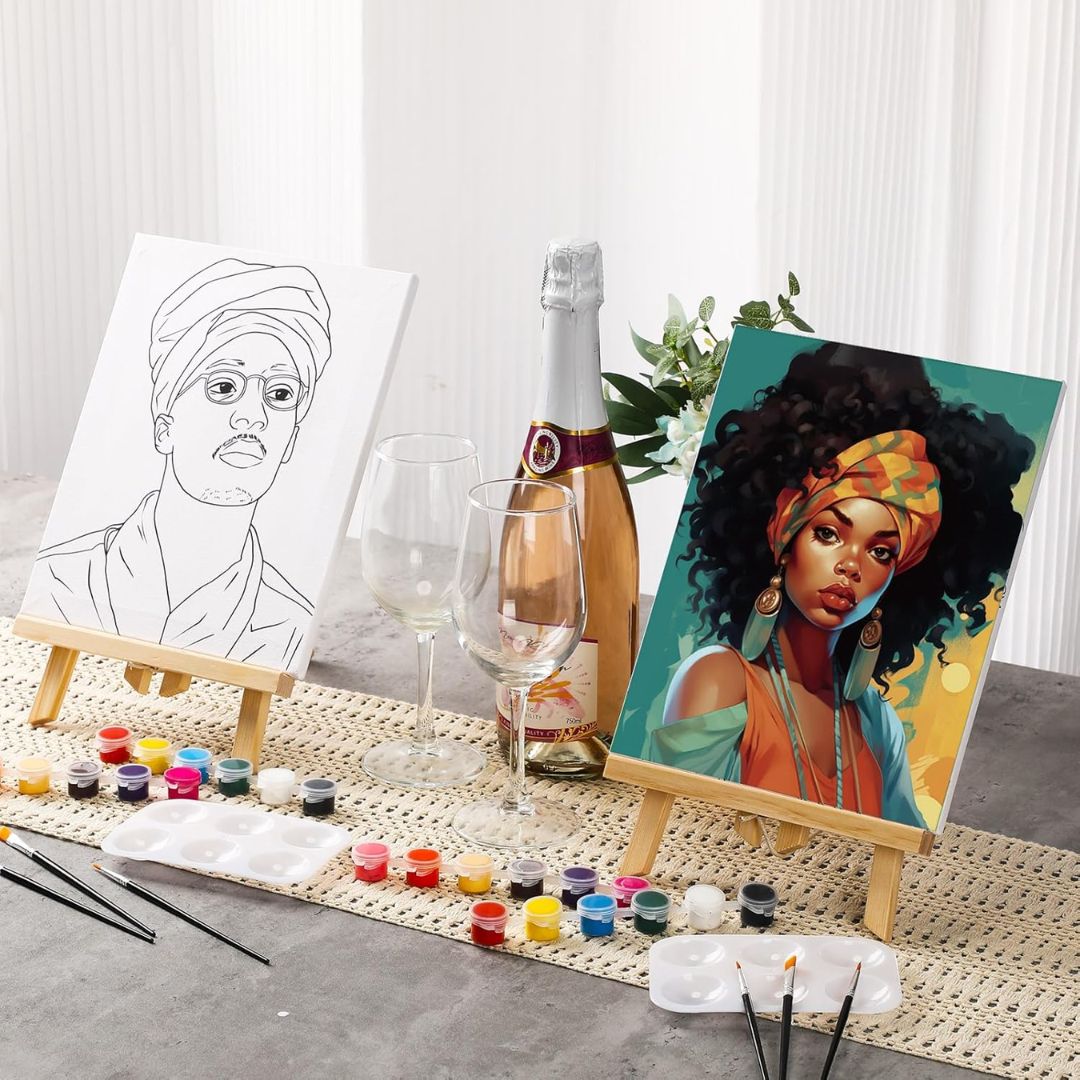 Artistic setup with a completed painting of a woman with a headscarf, a coloring book page, a bottle of champagne, and wine glasses on a textured surface.