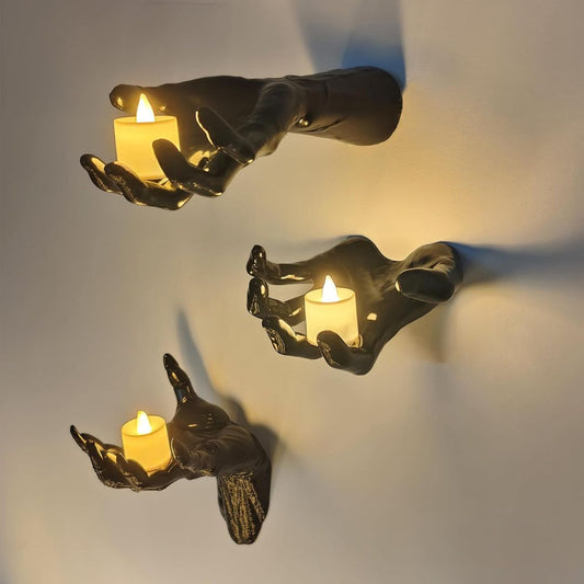 Three black hand-shaped candle holders with lit candles on a light gray background
