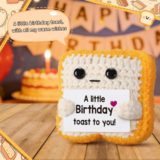 Crocheted toast character holding a birthday card with a birthday cake in the background