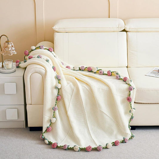 Cream crochet blanket with pink and white rose trim draped over a living room sofa
