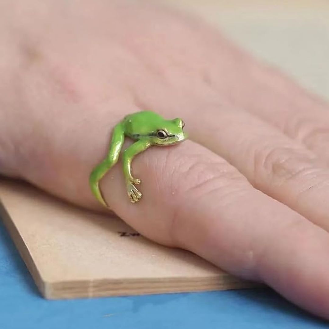 Green frog ring on a person's finger with a wooden block and blue surface in the background