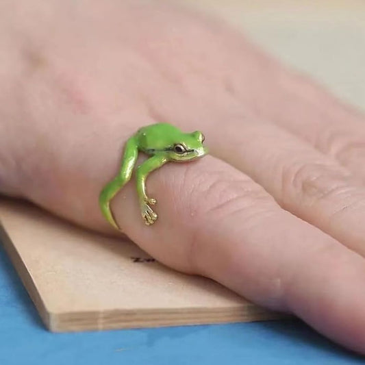 Green frog ring on a person's finger with a wooden block and blue surface in the background