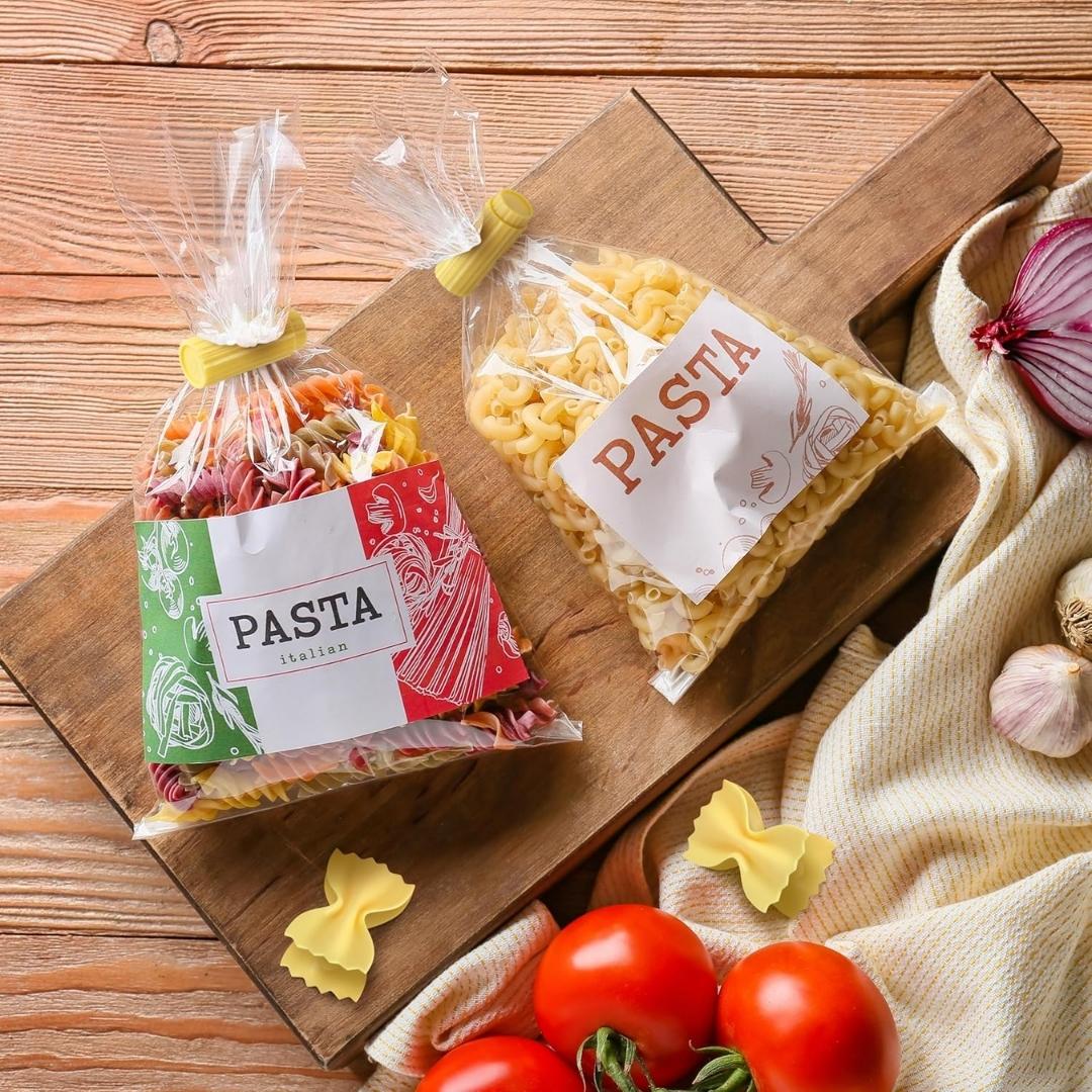 Two packages of pasta on a wooden board with tomatoes and garlic.