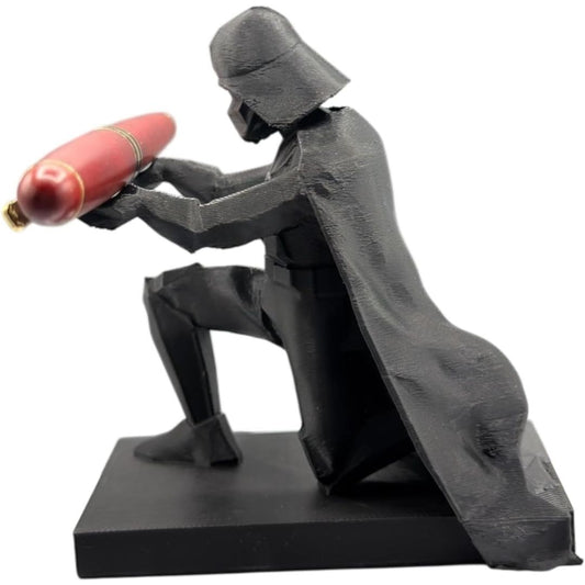 A Darth Vader pen holder figurine kneeling and holding a red pen, mounted on a black base against a plain white background.