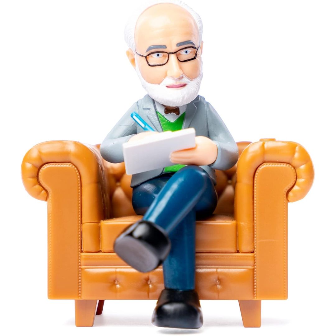 Figurine of a male therapist with glasses sitting on an orange chair holding a pen and paper.