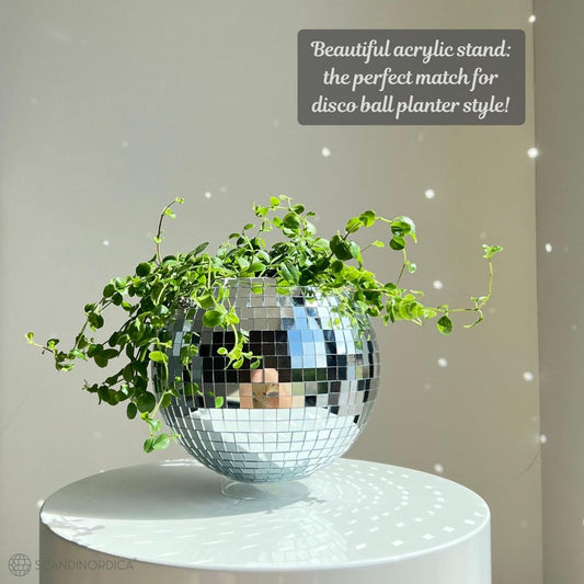 A disco ball hanging planter with a decorative plant inside on a white circular table