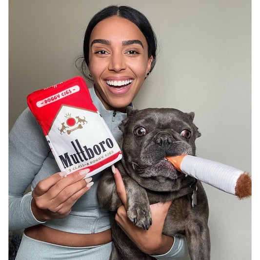 A woman holding a dog and a Muttboro dog cigarettes plush toy