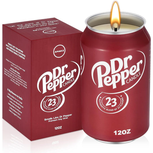 A Dr Pepper branded 12oz candle shaped like a can, shown lit with a visible flame, next to its matching red box. The can and box are dark red with white Dr Pepper branding and circular '23' graphics.