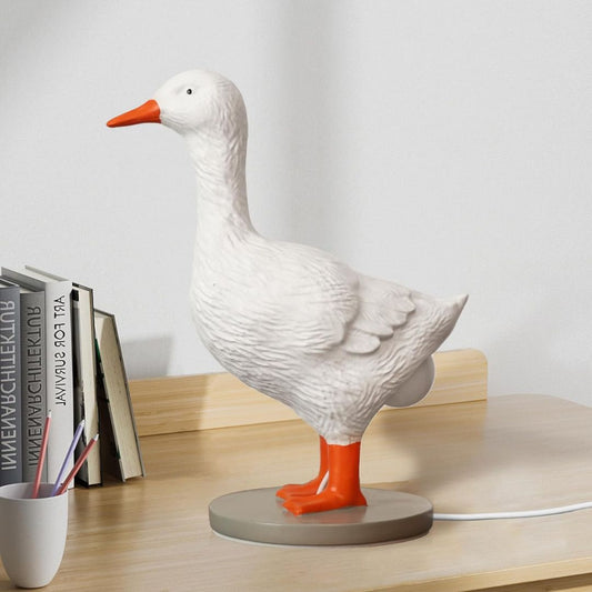 White goose figurine lamp with orange feet and beak on a wooden surface