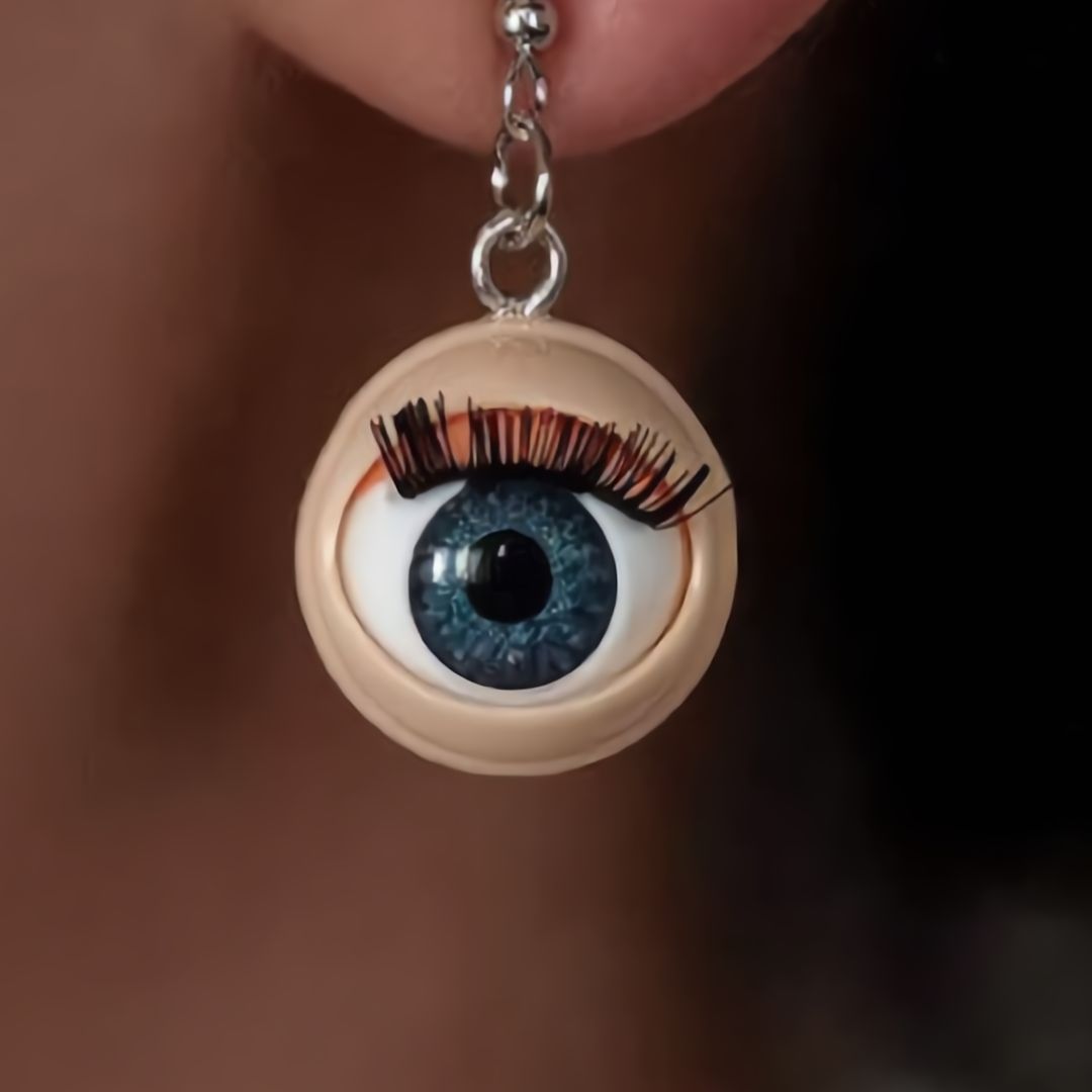 Eyeball-shaped earring with blue eye detail worn on an ear.