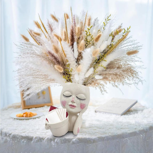 A plant pot shaped like a woman's head and shoulders with a dried flower arrangement coming out of her head that looks like hair.