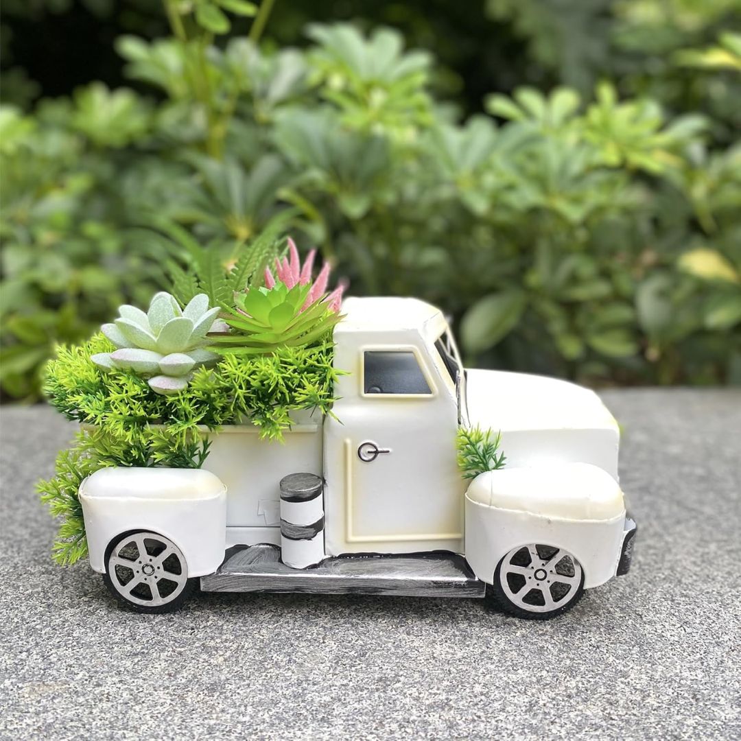 White model pickup truck with fake plants on a gray surface with greenery in the background