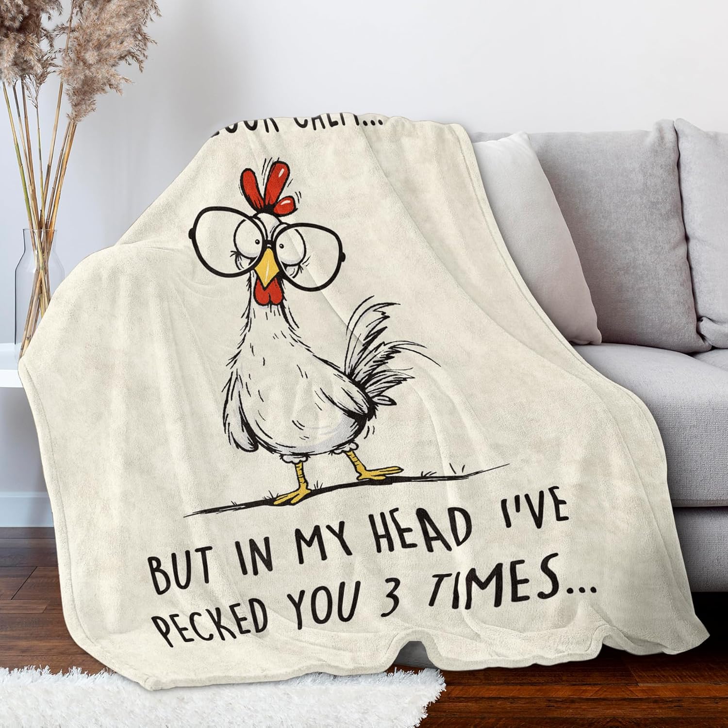Blanket with a cartoon rooster and humorous text on a couch in a living room.
