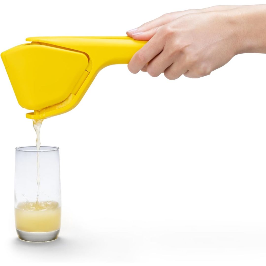 Yellow fold-flat citrus juicer squeezing fresh juice into a drinking glass