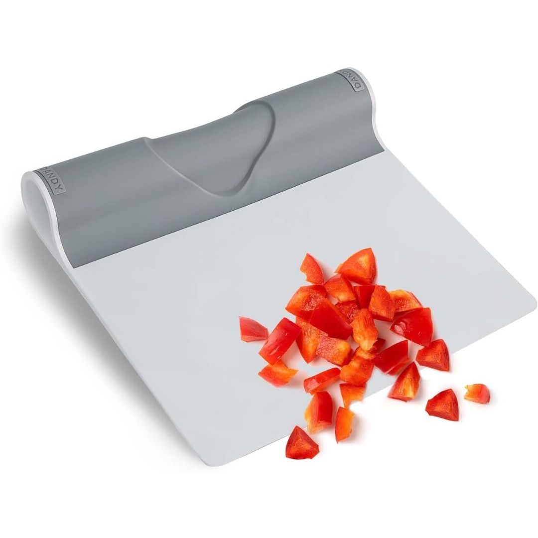 Flexible folding food scooper with chopped red pepper, designed for scraping and transferring ingredients from a cutting board