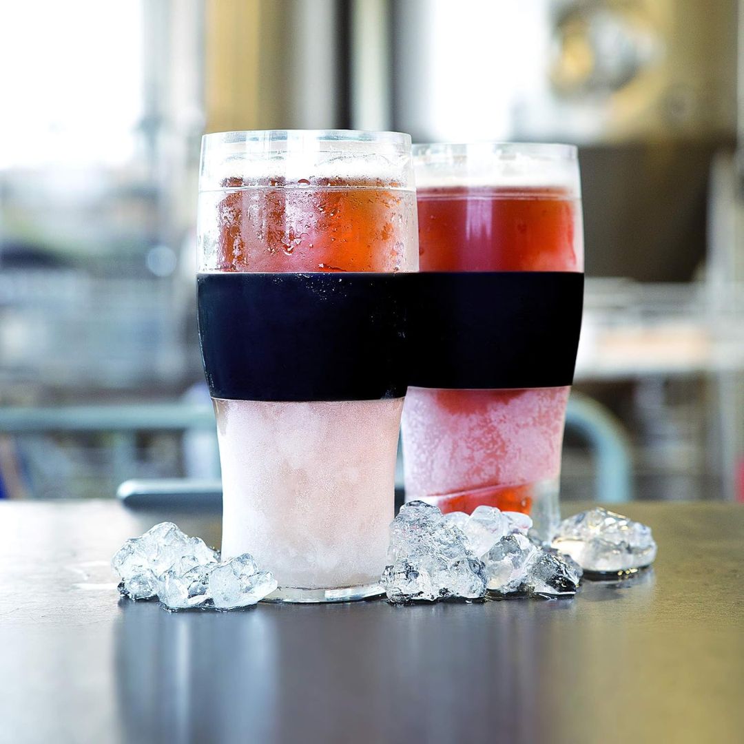 Two insulated freezable beer glasses of iced drinks with a black grip band on a reflective surface.