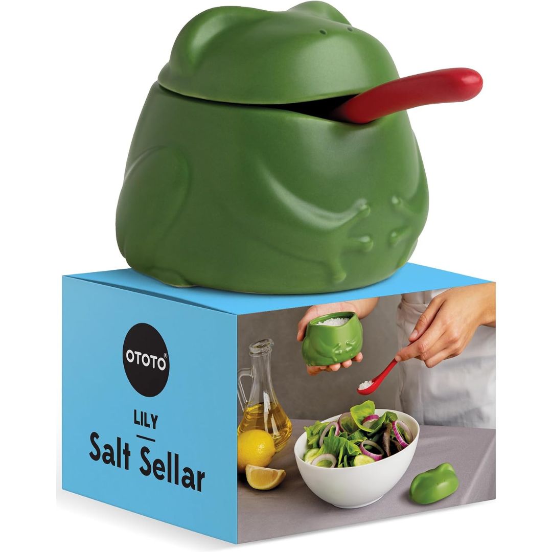 A green frog-shaped salt container with a red spoon resting inside, displayed on top of its blue retail box. The box is branded OTOTO and reads 'Lily Salt Sellar'.