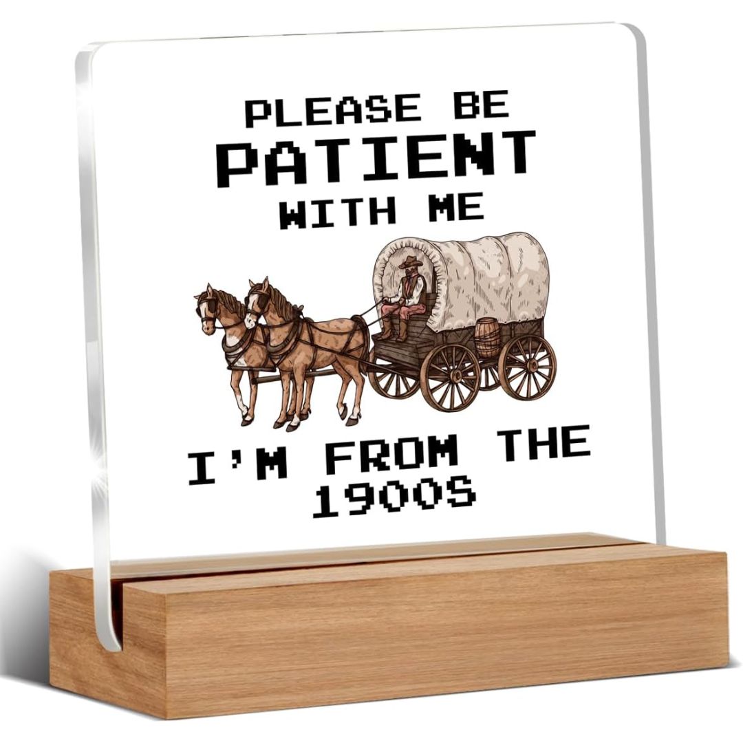 A funny glass and wood sign with text reading 'Please be patient with me I'm not the 1900s' on a white background