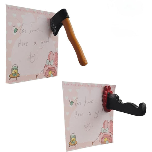 Two novelty magnets shaped like a small axe and a bloodied knife, shown attached to pink heart-patterned note cards. 