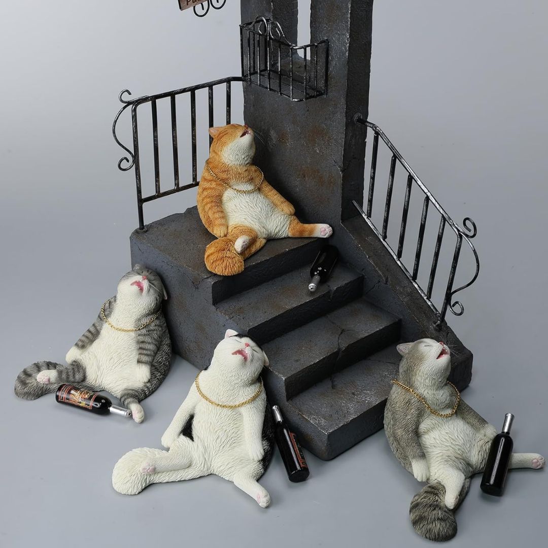 Four resin drunk cat figurines posed around a miniature dark staircase set on a light gray background. One orange-and-white cat sits on the stairs, while three white-and-gray cats lie on the floor beside small bottles.