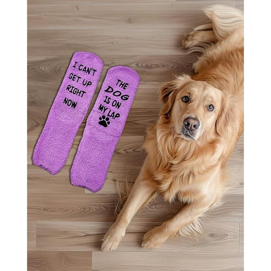 Two purple socks with humorous text next to a golden retriever on a wooden floor.