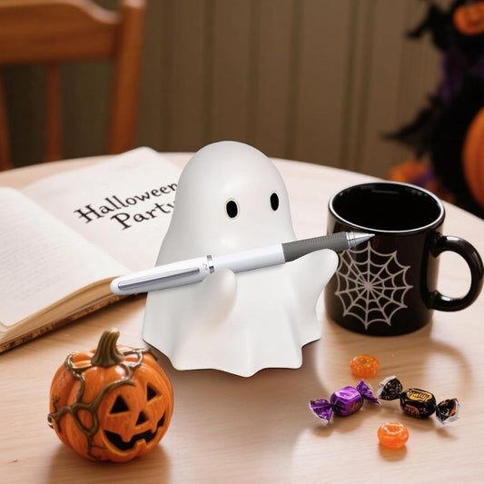 Ghost-shaped pen holder with a pen, Halloween-themed mug, pumpkin, and candy on a table.