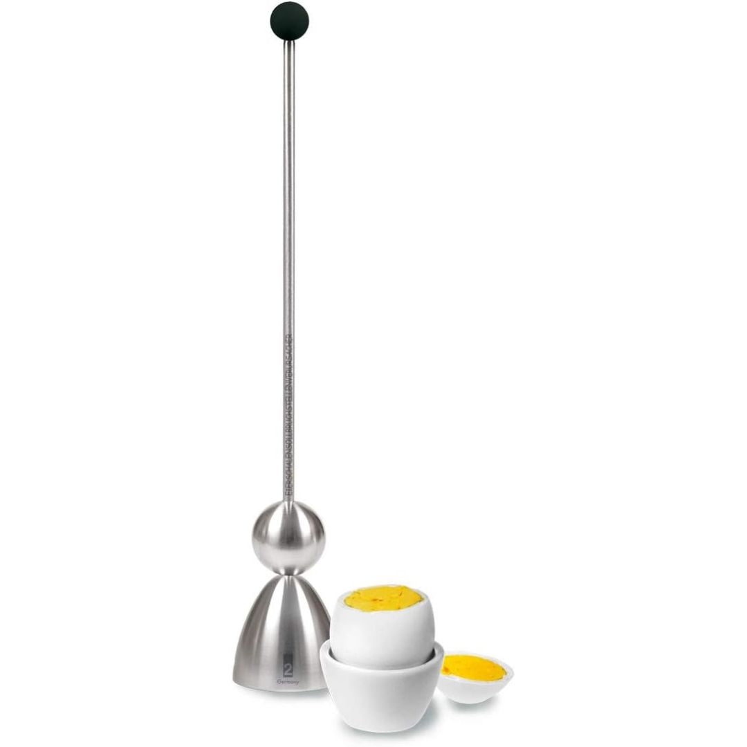 A stainless steel egg topper with a long metal rod, ball-shaped head, and a small white bowl containing a cooked egg with the top removed, shown on a plain white background.