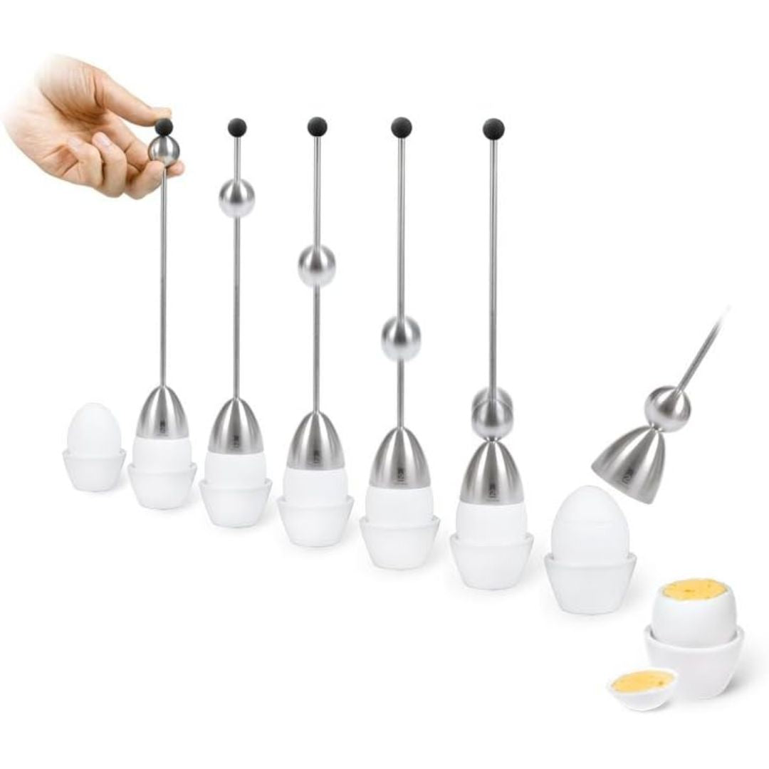 A set of stainless steel egg toppers with a number of cooked eggs in egg holders. A human hand is visible holding one of the long metal tools, and two cooked eggs are shown at the bottom right.
