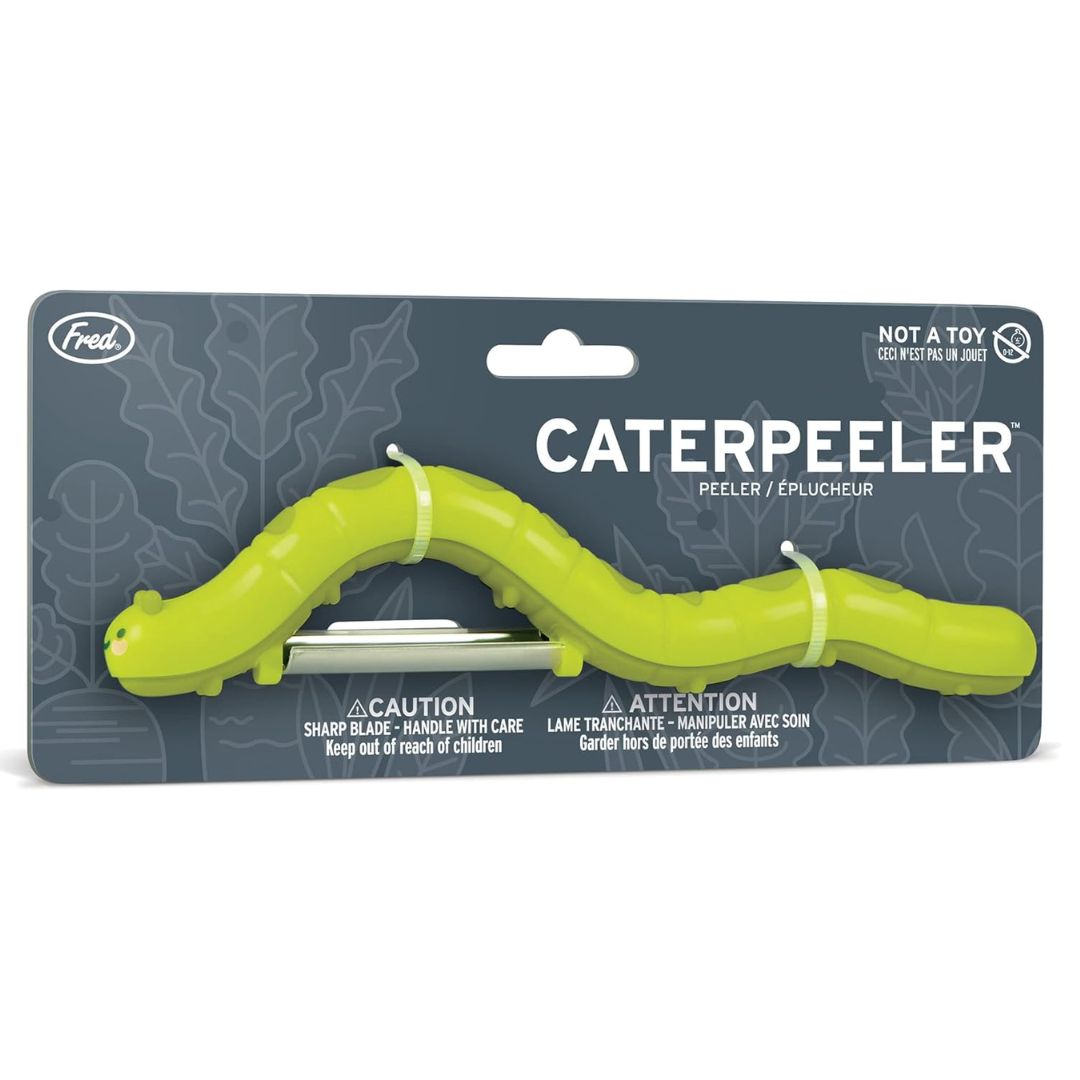 A green caterpillar-shaped peeler tool in retail packaging on a white background. The card shows the brand Fred.